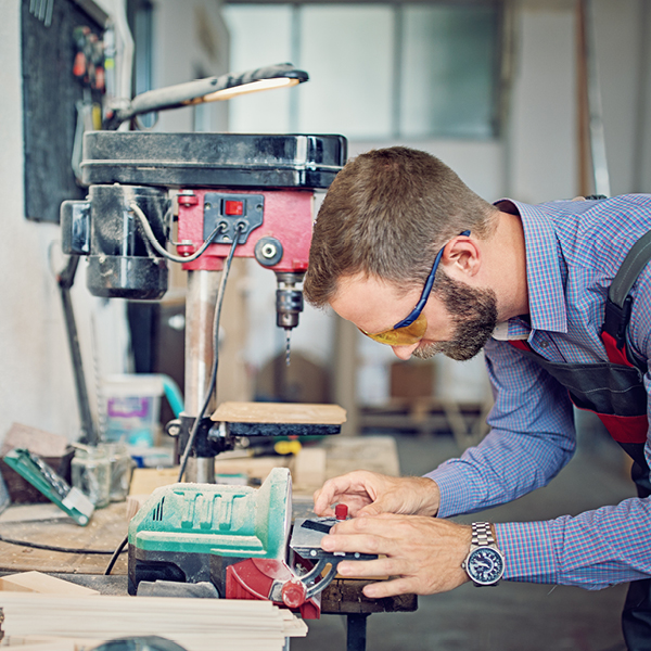 A man using a drill press in a shop environment